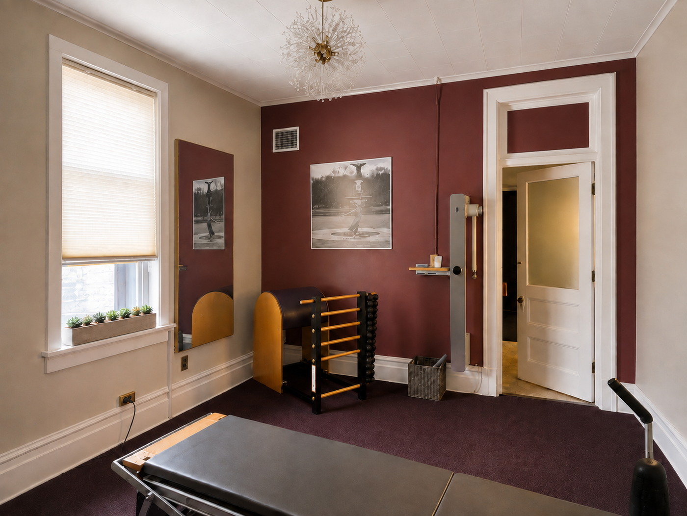 A second view of the GLOW Body studio: the ladder barrel and Cadillac tower against the oxblood wall, with the window and the original panelled door